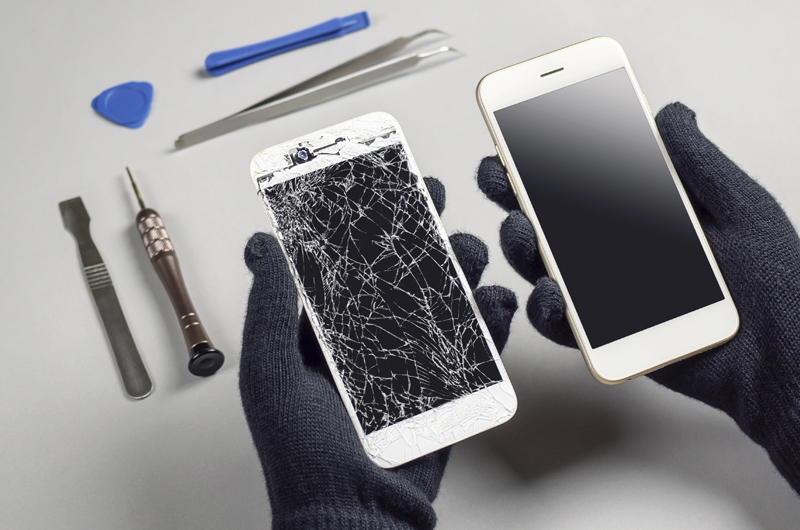 Zwei Smartphones, eines mit zersprungenem Display, Reparaturwerkzeuge im Hintergrund.